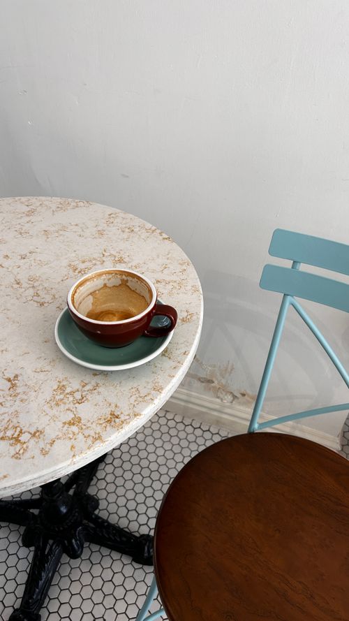 Free A minimalist cafe setting featuring an empty coffee cup on a marble table next to a blue chair. Stock Photo