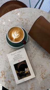A cup of latte with latte art beside a book on a café table.