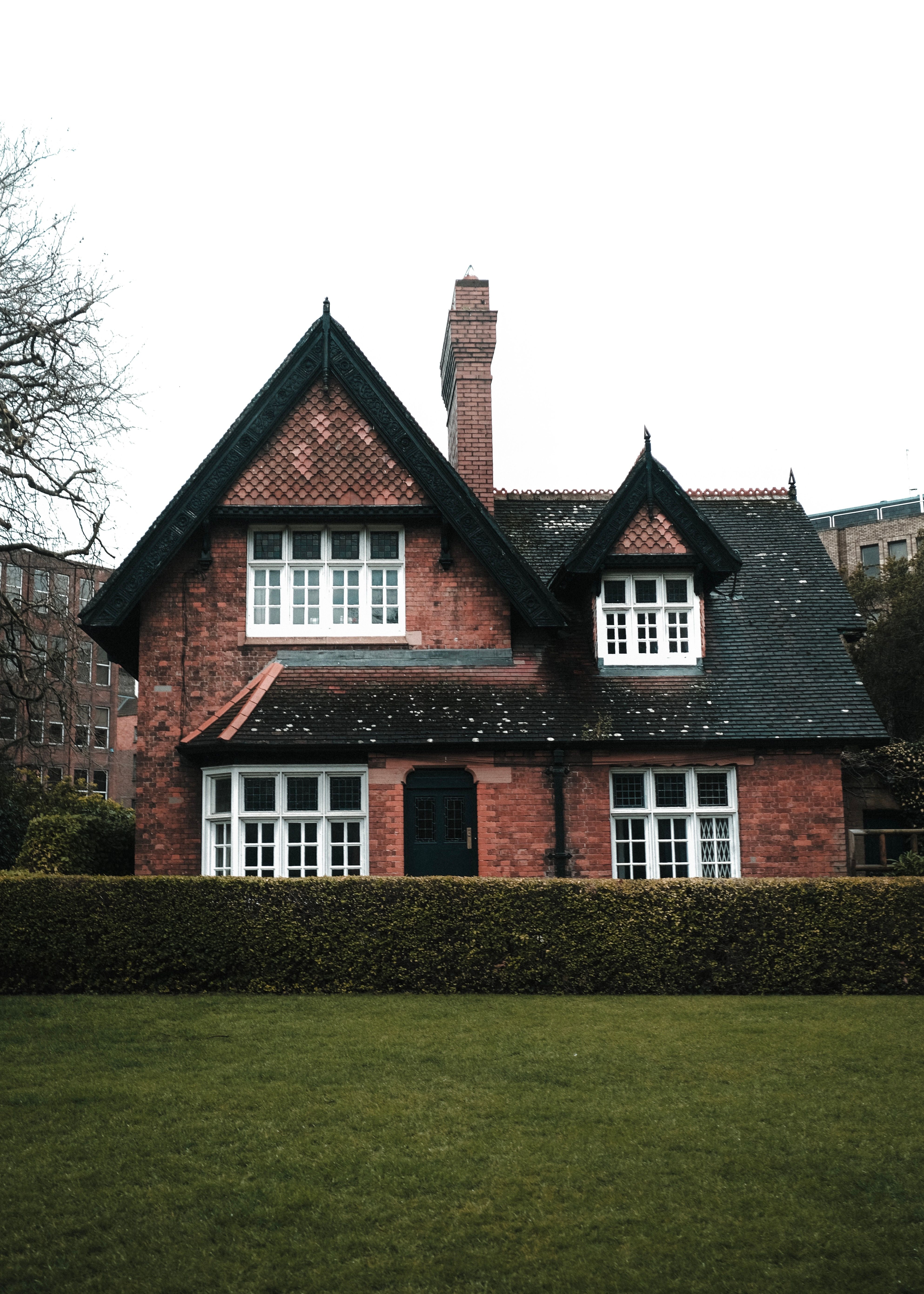 Red-brick detached Arts and Crafts style house behind hedge and lawn