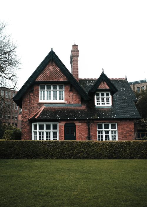 Free Classic red-brick house surrounded by lush greenery and hedge in a village setting. Stock Photo