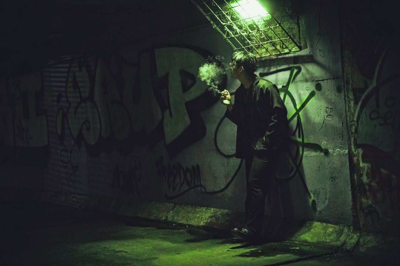 a young man stands in a dark tunnel illuminated by green light surroun