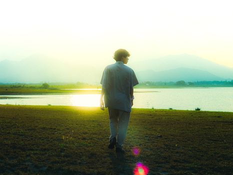 A young man walks by a tranquil lake during sunset, embodying peace and reflection.