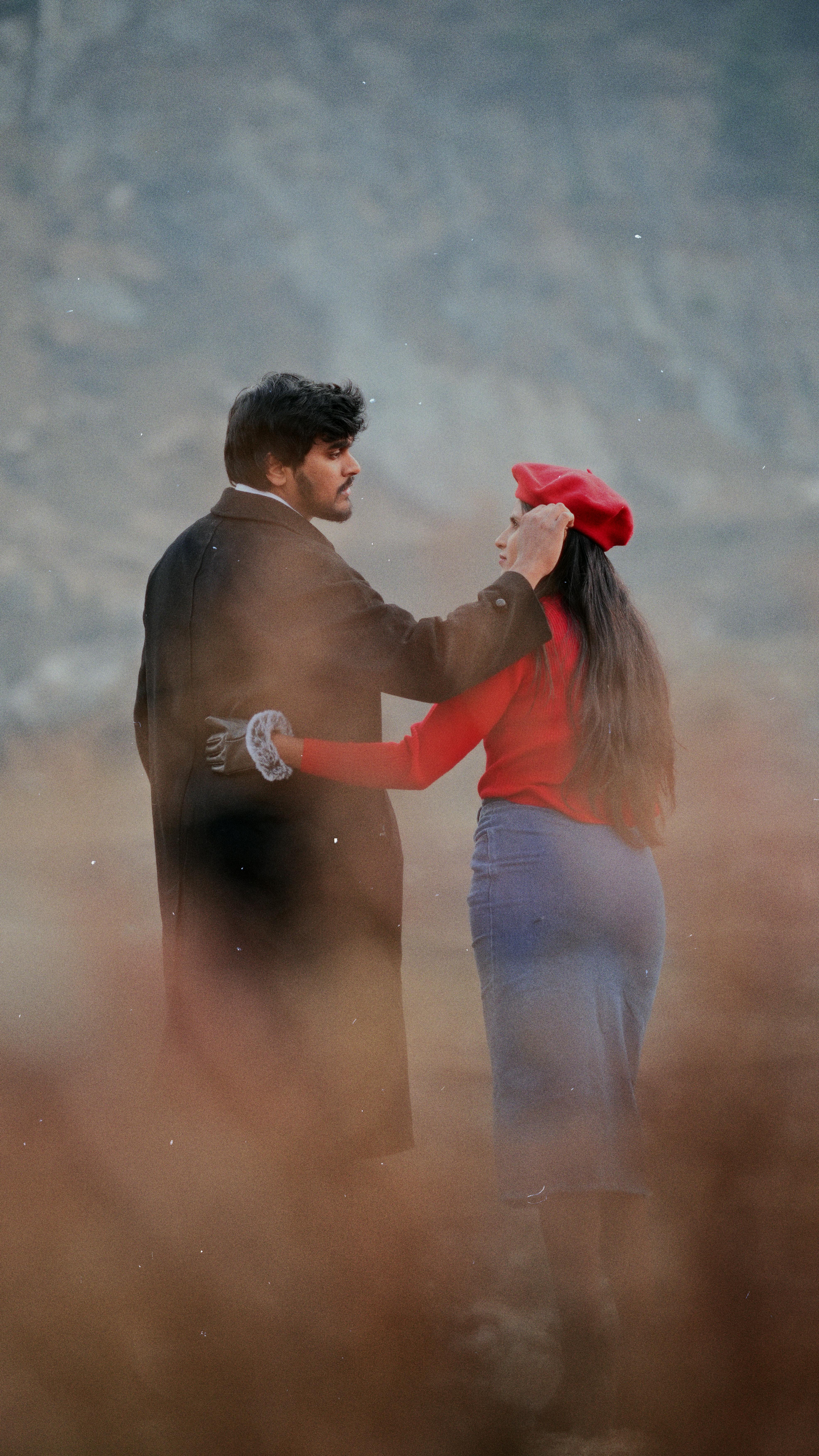 A couple shares a warm embrace amidst a stunning mountainous backdrop.