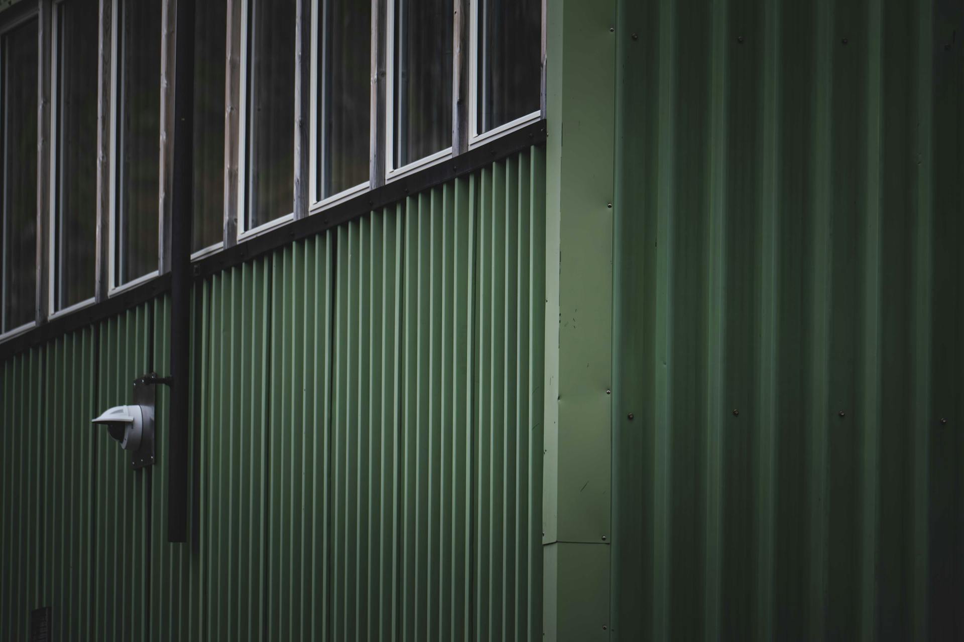 Dark green corrugated metal facade with windows and security camera.