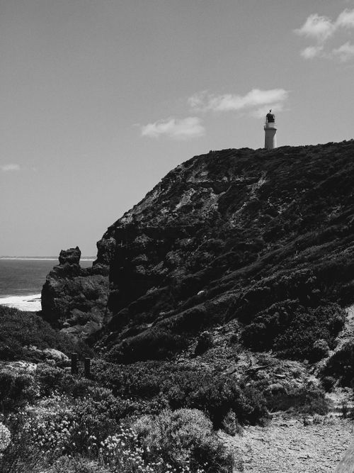 Free Dramatic black and white photo of a coastal lighthouse on a rugged cliff. Stock Photo