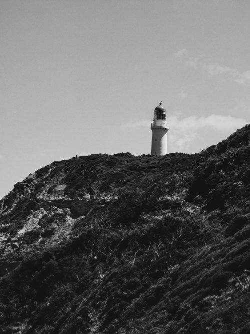 Free A striking black and white photo of a lighthouse standing on a rugged cliffside under a clear sky. Stock Photo