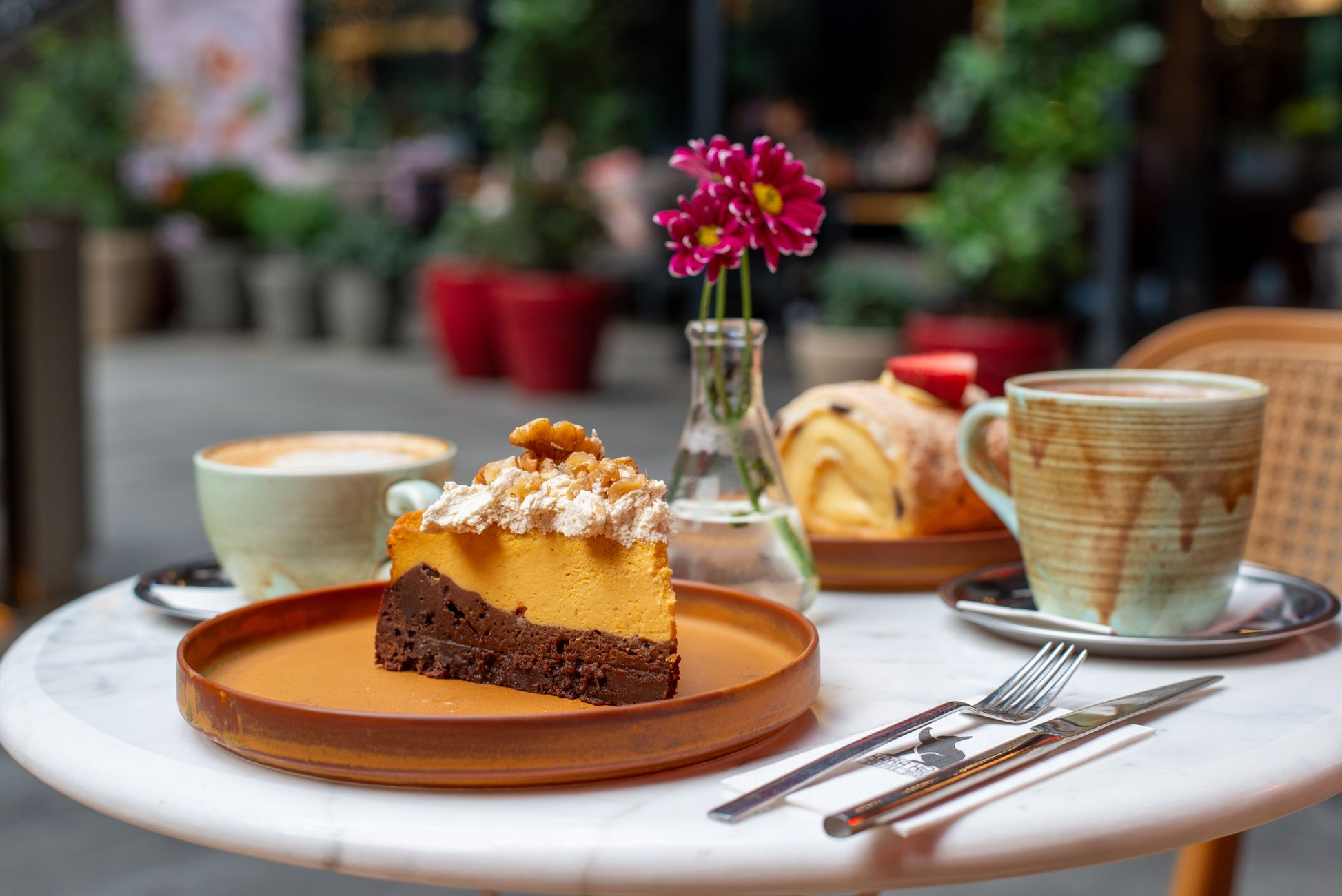 A charming café scene featuring desserts and coffee on a table with a vase of flowers.