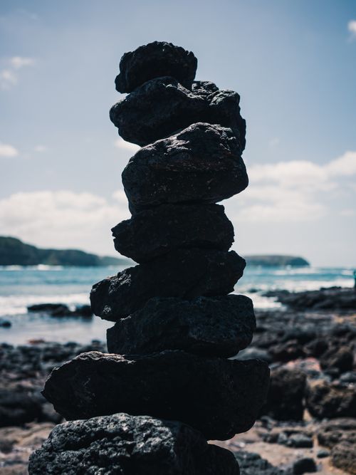 Free A stack of balanced stones on a rocky shore against a blue sea and sky. Stock Photo