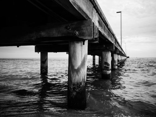 Free Black and white image of a wooden pier extending over the ocean, creating a dramatic and serene mood. Stock Photo