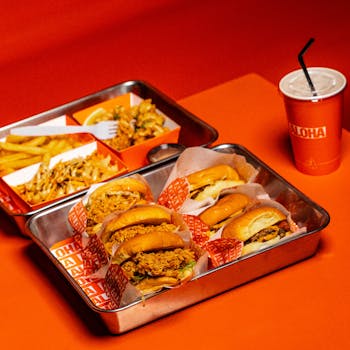 A vibrant display of burgers, fries, and a drink on an orange background.