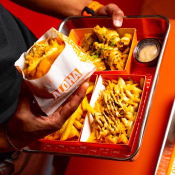 Close-up of a person holding a tray with fast food including burger and fries.