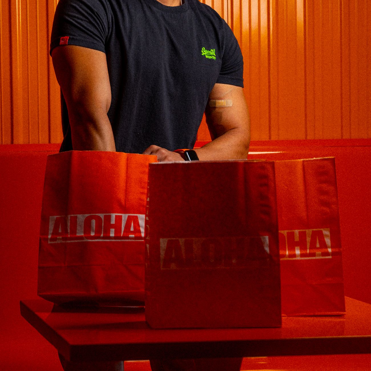 A man stands by three red paper bags labeled 'ALOHA' in a modern restaurant setting.