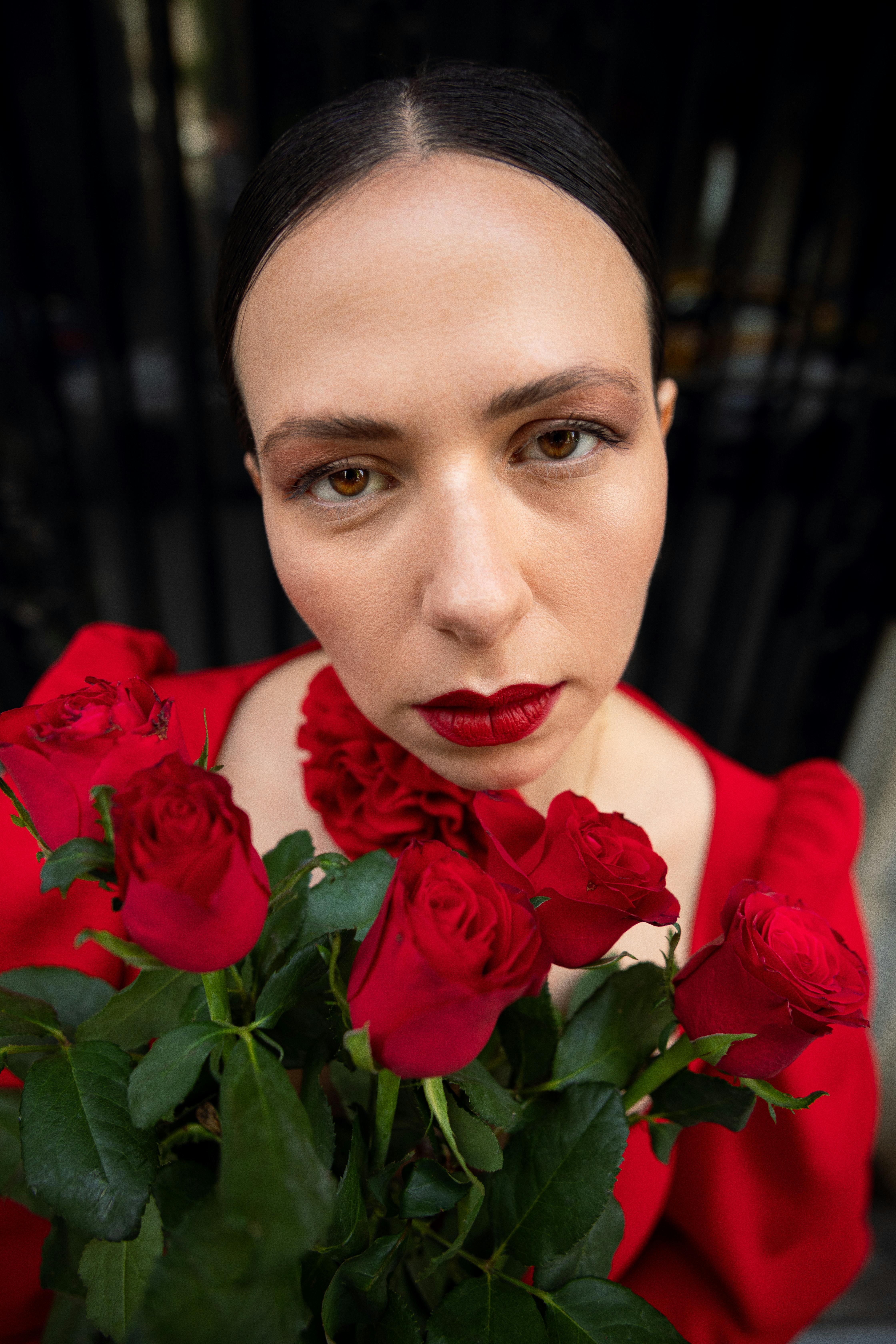 A woman in a red dress holds red roses, exuding elegance and romance.