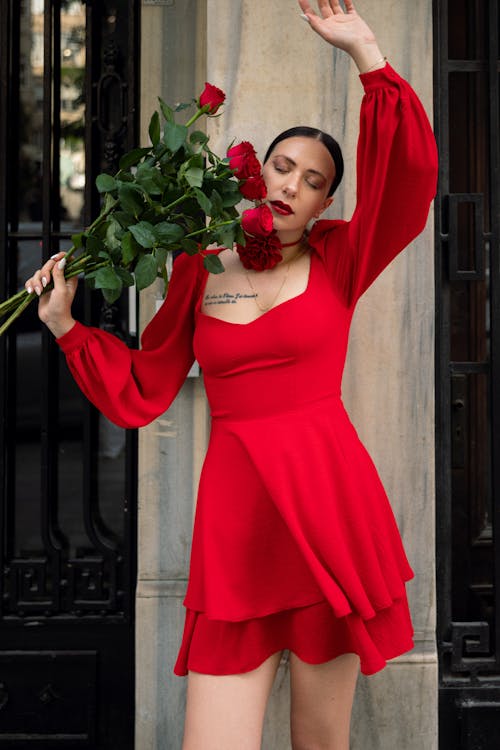 Young Woman Wearing a Red Dress, Red Lipstick and Holding a Bouquet of Red Roses 