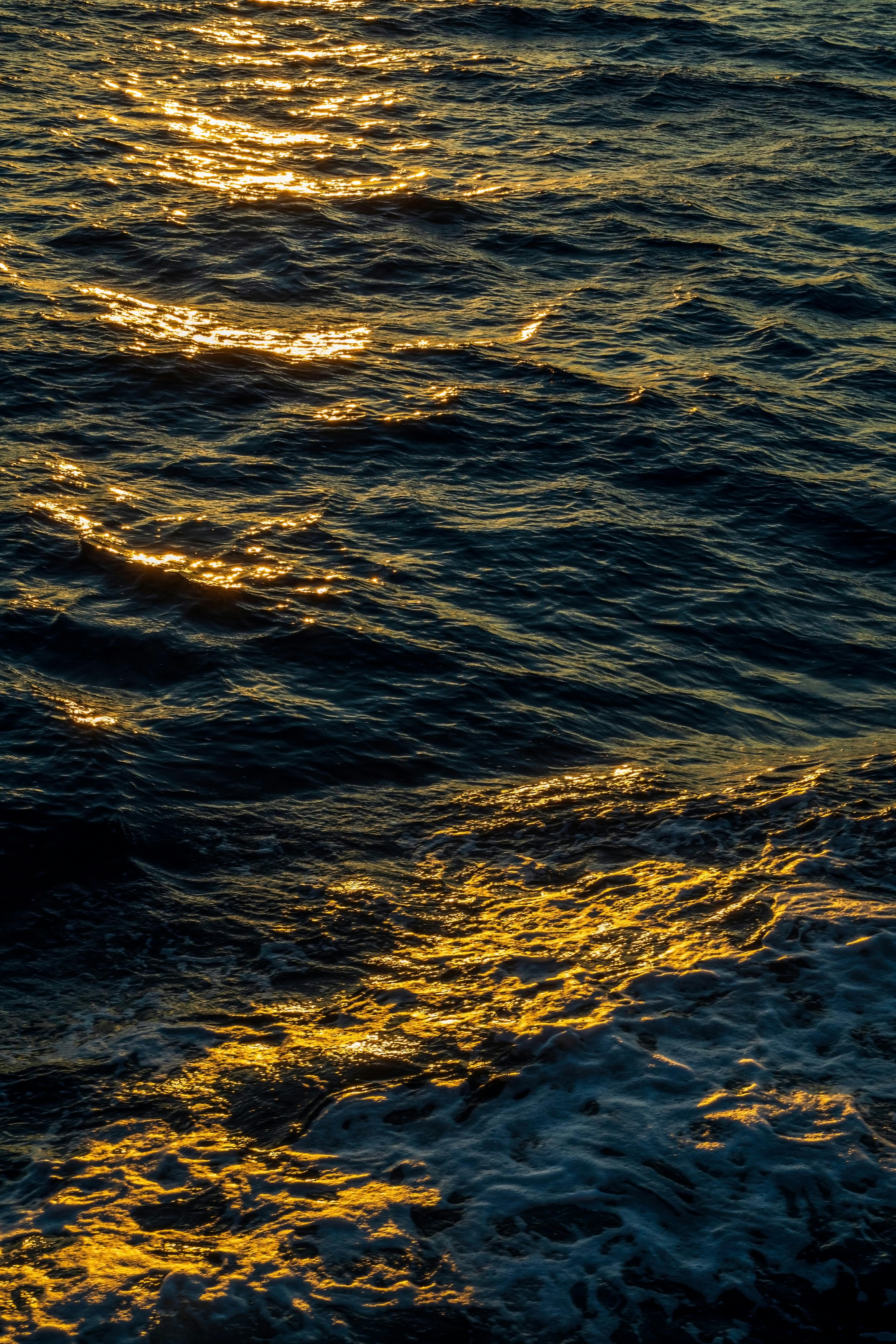 Waves reflecting golden sunlight during sunset, capturing serene ocean beauty.