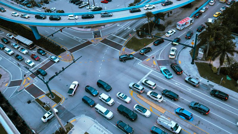 Aerial view of a busy urban intersection filled with cars and traffic under a blue overpass.