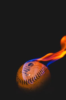 Close-up shot of a baseball engulfed in vivid orange flames against a dark background.