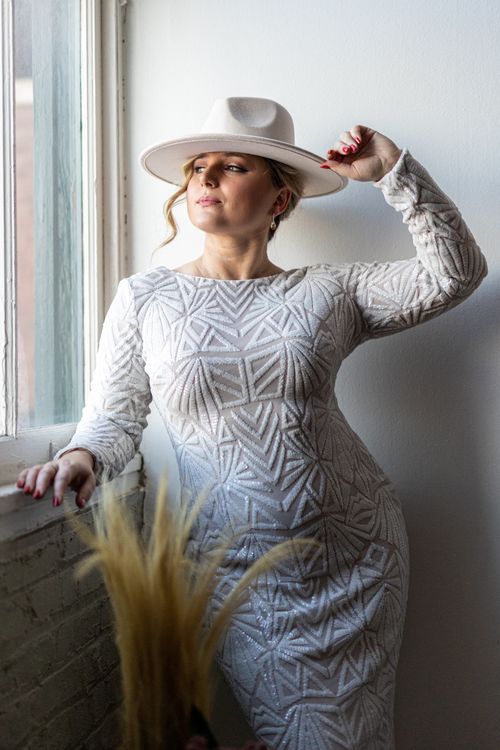 Free Stylish portrait featuring a woman in a white dress and hat, captured in natural light by a window in Chicago. Stock Photo