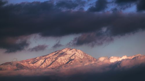 Free A picturesque snowy mountain peak enveloped by dramatic clouds at sunset. Stock Photo