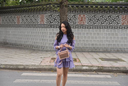 A woman in a purple dress and heels is standing on the street