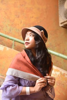 Elegant portrait of a woman in urban setting wearing a hat and scarf, exuding fashion-forward style.