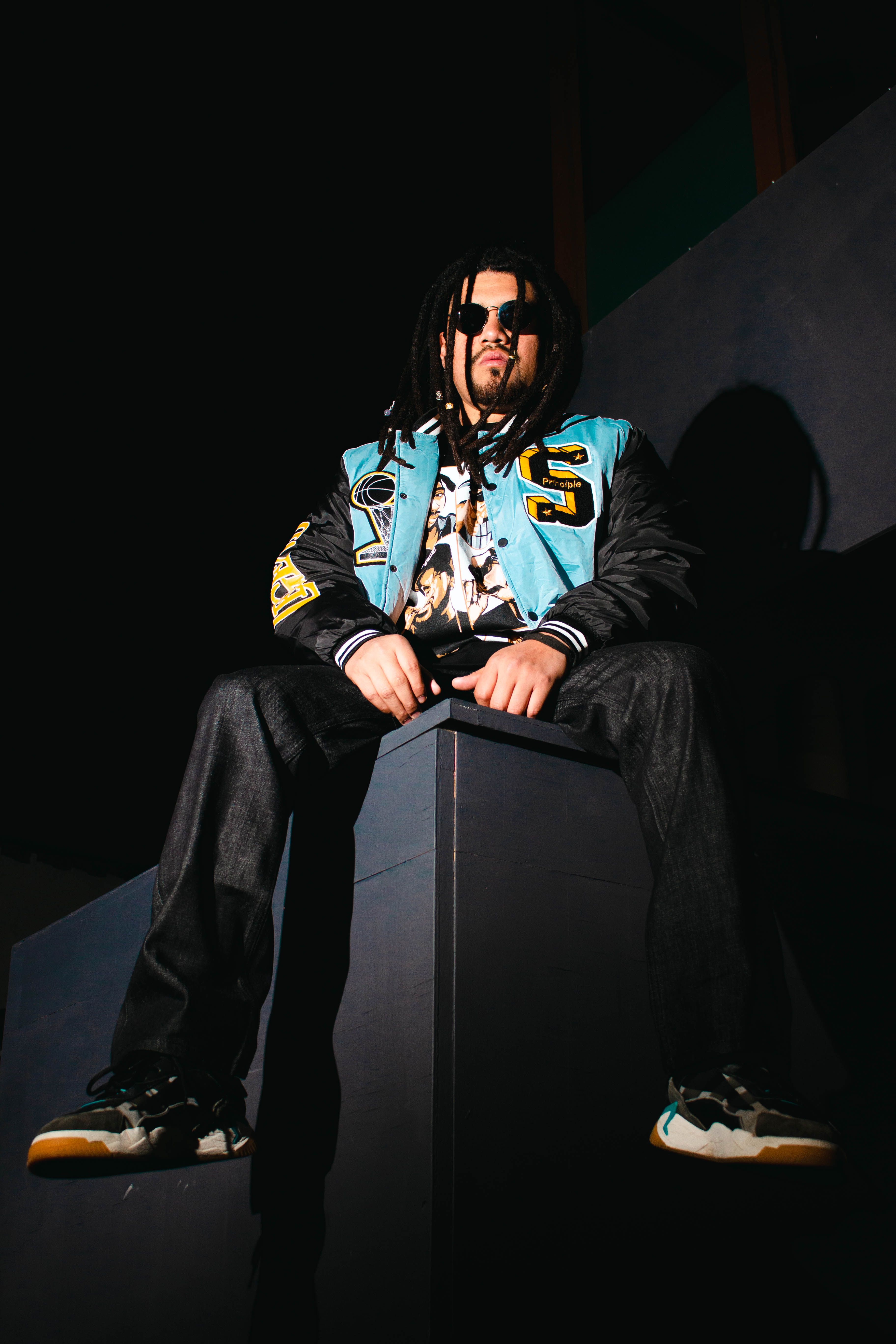 Stylish man with dreadlocks and sunglasses posing in urban setting, showcasing modern fashion vibes.
