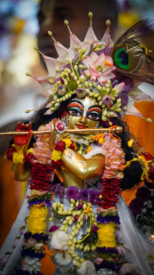 Free Intricate golden Hindu deity figurine adorned with flowers and vibrant peacock feather. Stock Photo