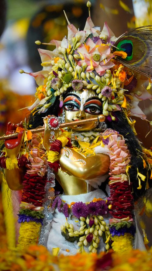 Free Vibrant statue of Hindu God Krishna adorned with flowers and golden details, symbolizing spiritual culture. Stock Photo