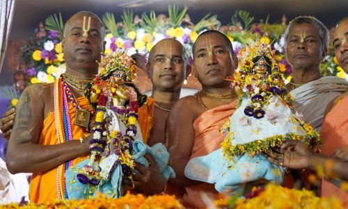 Free Group of Indian men in traditional clothing holding decorated Hindu deity figurines during a religious ceremony. Stock Photo