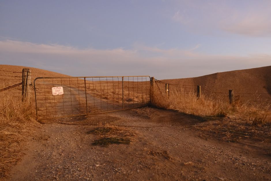 empty rural gravel driveway with open gate after tow truck departs morning light
