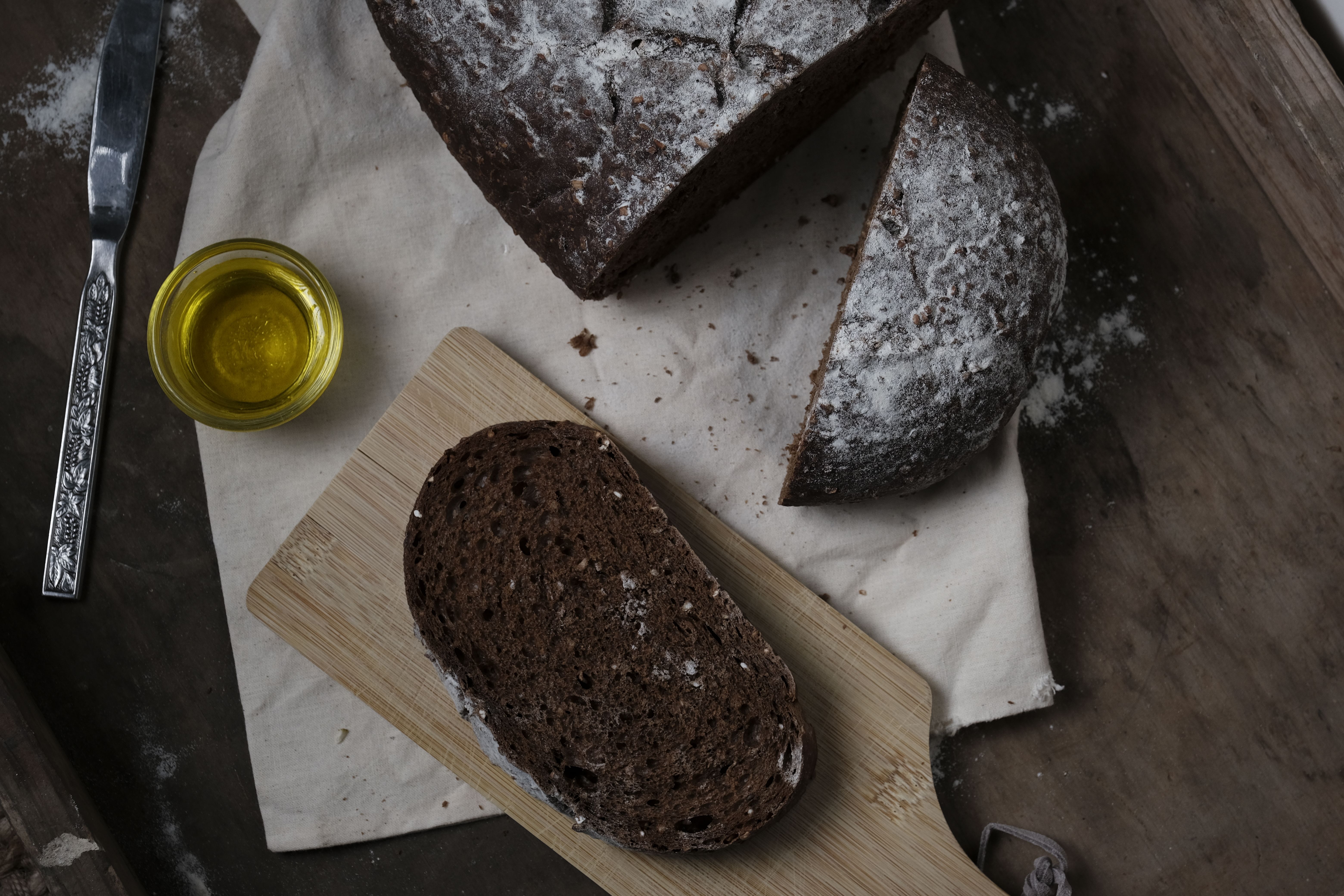 A rustic slice of dark bread with olive oil on a wooden board. Perfect for food photography enthusiasts.