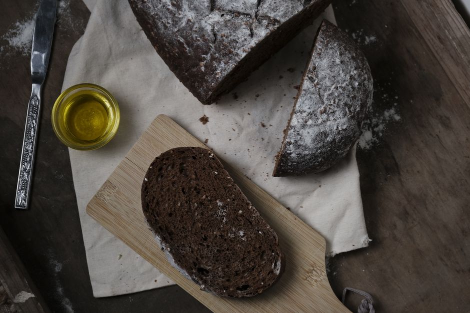A rustic slice of dark bread with olive oil on a wooden board. Perfect for food photography enthusiasts.