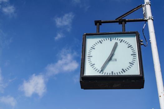 Outdoor analog clock against a bright blue sky in Krynica-Zdrój, Poland.