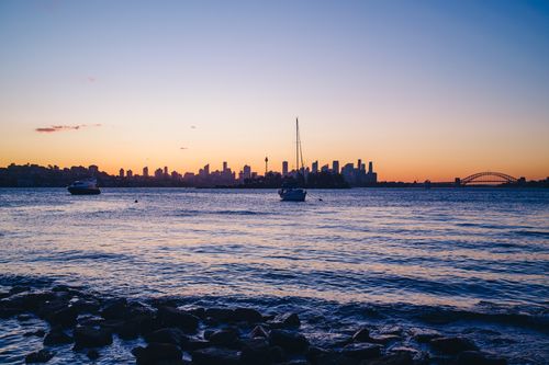 Free A stunning sunset view of Sydney Harbor with the city skyline and boats. Stock Photo