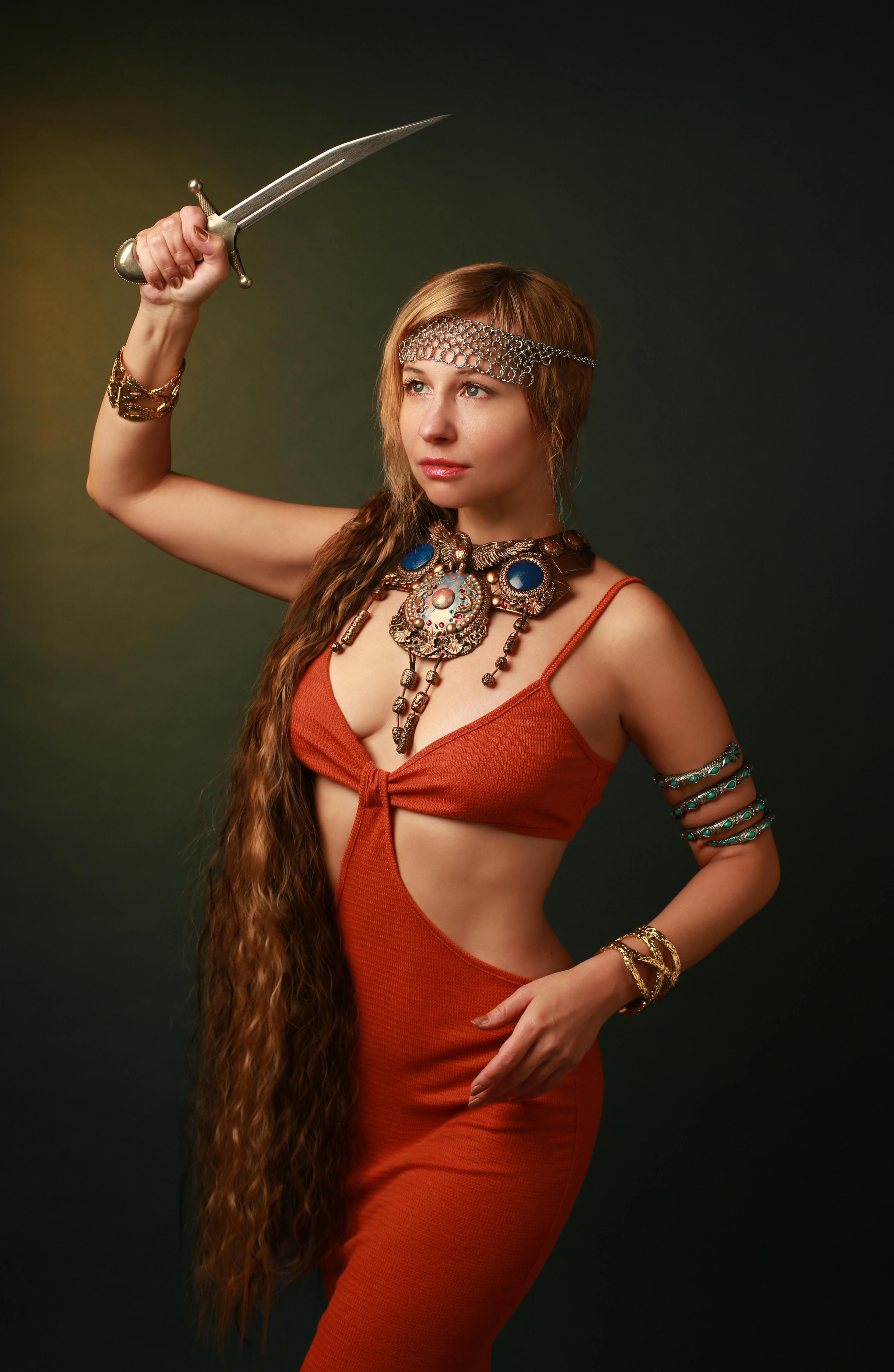 Stunning portrait of a woman in a red dress holding a dagger, showcasing fashion and jewelry.