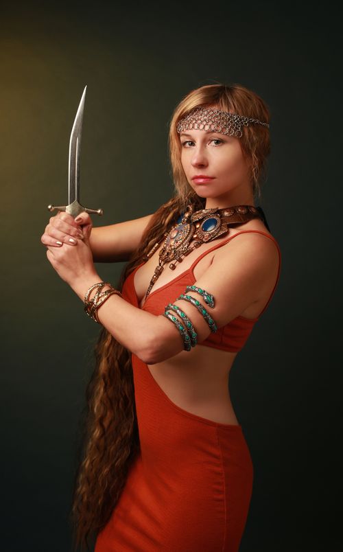 Free Stunning fashion portrait of a woman in red dress holding a dagger, showcasing jewelry. Stock Photo