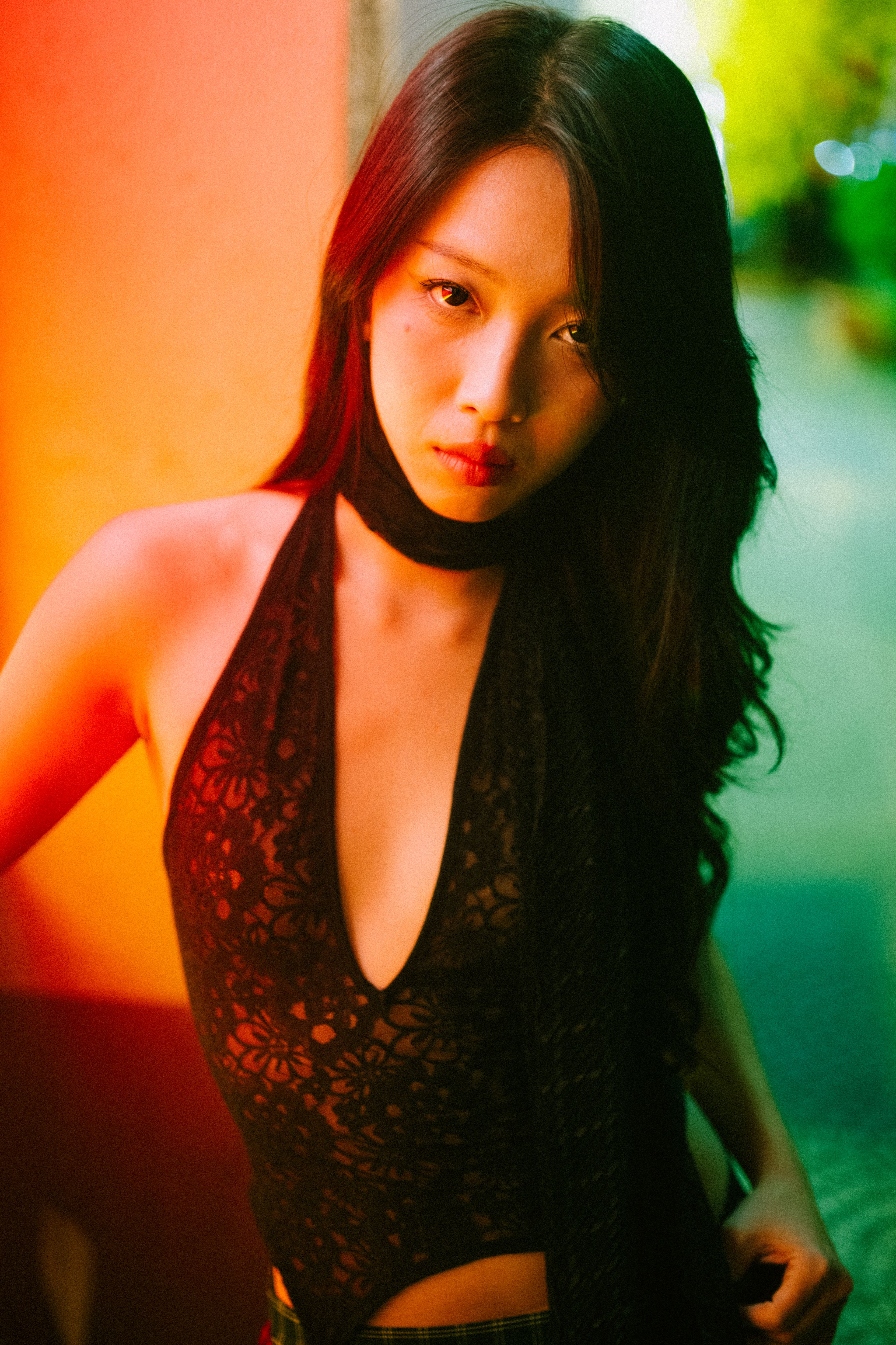 Stylish portrait of an Asian woman in designer lace bodysuit with vibrant lighting.