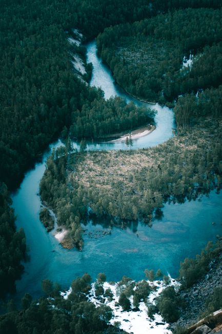 A stunning aerial view showcases a winding river surrounded by a snowy forest landscape during winter.