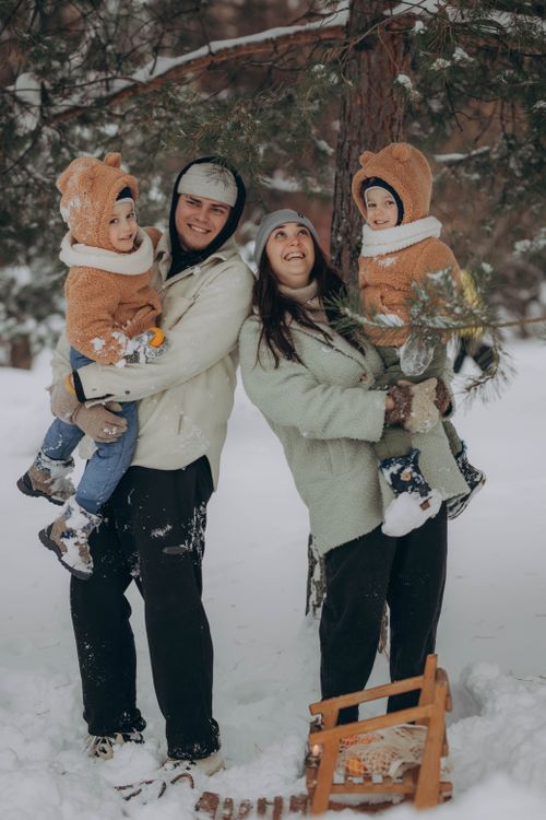 Free A joyful family with children in winter attire enjoying the snow by a conifer tree. Stock Photo