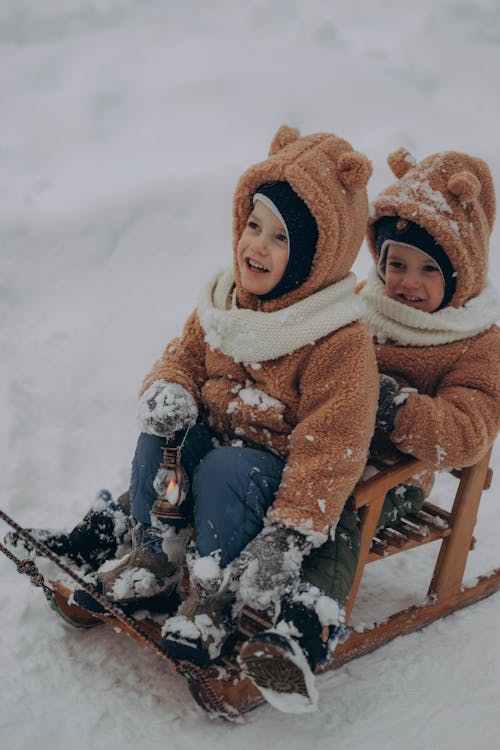 Two Little Children Sitting on Wooden Sled and Smiling 