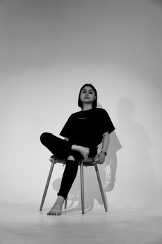 Monochrome portrait of a woman sitting barefoot on a chair, showcasing modern fashion and elegance.