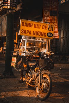 A street food vendor using a motorbike to sell bánh hạt dẻ sapa nuong in a Vietnamese town.