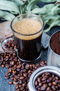 A glass of freshly brewed coffee surrounded by coffee beans and ground coffee.
