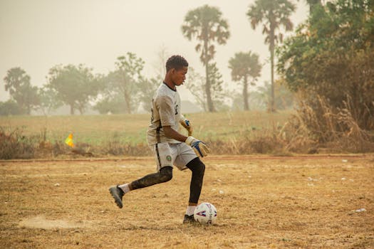 Young boy in a soccer uniform kicking a ball in a grassy field, showcasing athletic skills.