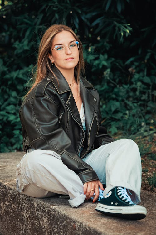 Free Female Model Wearing a Black Leather Jacket Sitting on a Stone Wall Stock Photo