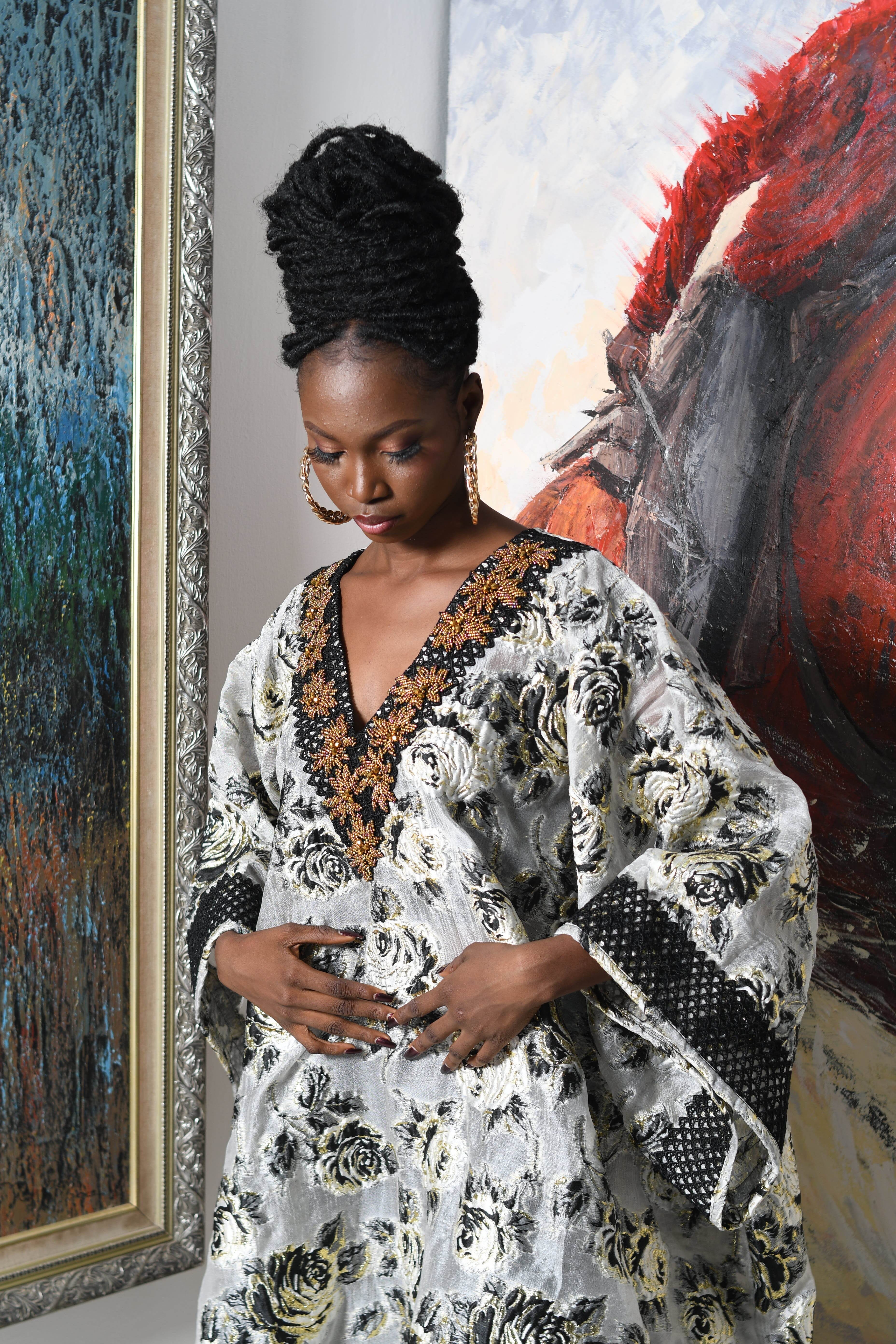 Stylish portrait of a woman in a detailed patterned dress, standing by abstract paintings.