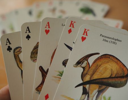 Close-up of dinosaur-themed playing cards featuring aces and kings in a poker hand., free online jigsaw puzzle on JigsawPuzzlesFreeOnline.org