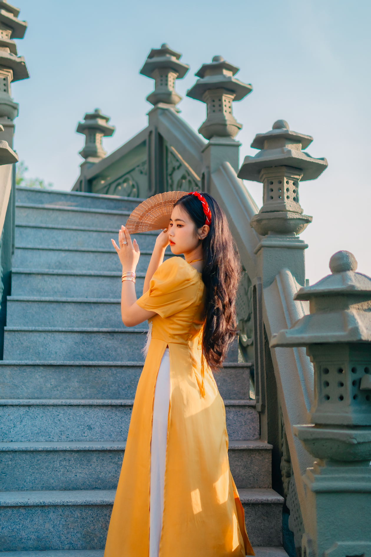 Woman in a yellow ao dai, a traditional long tunic, holding a fan on stone stairs