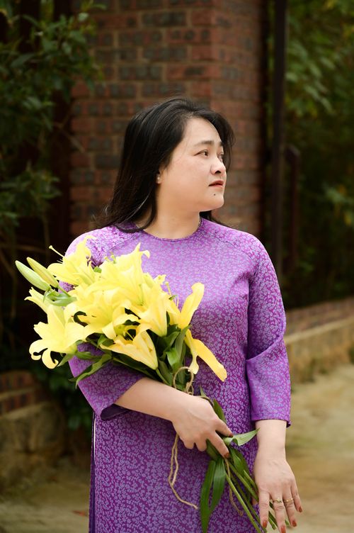 Free Portrait of an Asian woman in a purple dress holding yellow lilies outside. Elegant and serene. Stock Photo