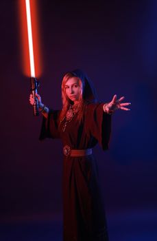 A mysterious woman in a dark robe poses confidently with a glowing red light sword against a blue background.